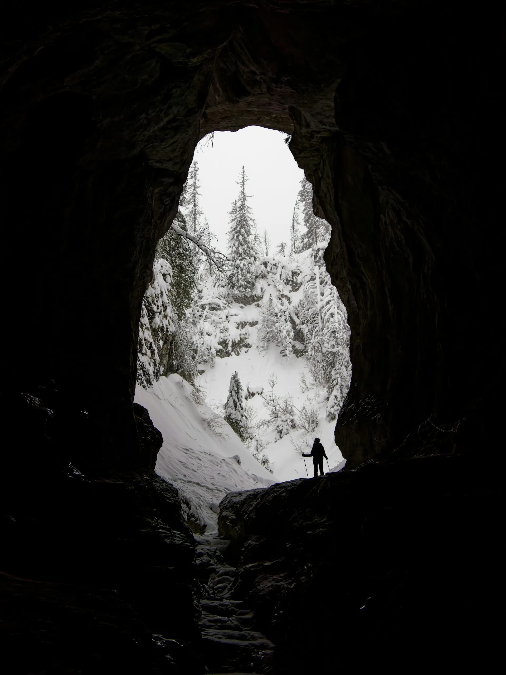 Hiker standing in the mouth of a snowy cave in a winter forest